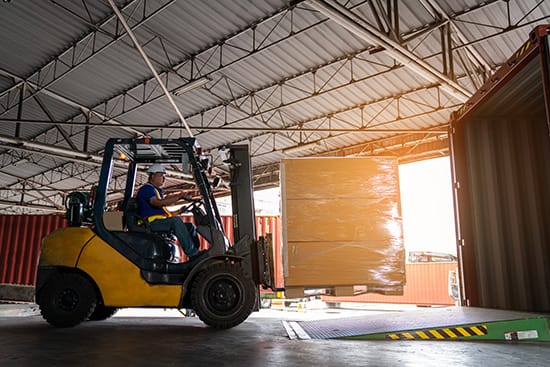forklift driver loading pallet of boxes on truck dock